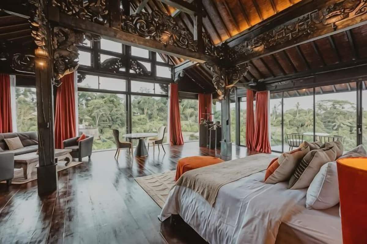 A spacious room with a large bed, a dining table, and chairs, a sofa, and a view of the outdoors through large windows.