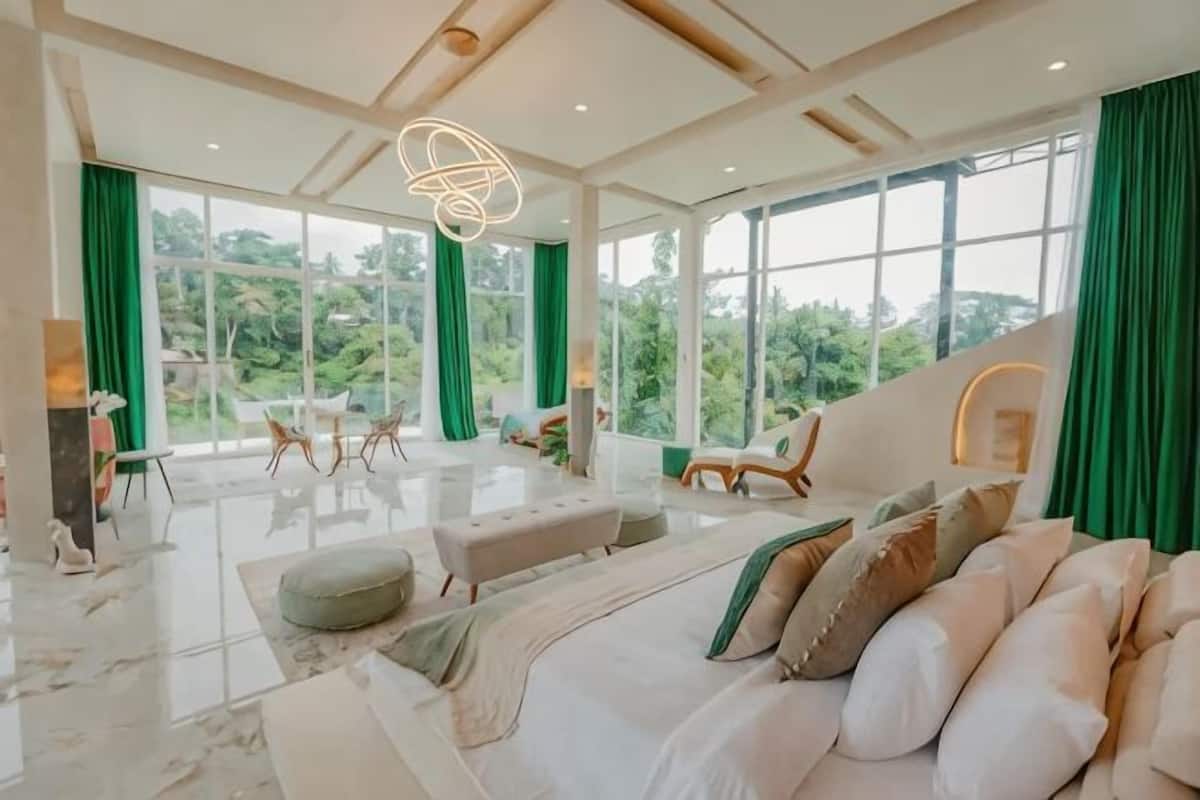 A spacious room with a large bed, a seating area with a sofa and chairs, and large windows offering a view of greenery.