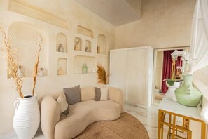 A living room with a curved sofa, a white vase with branches, a wooden table, and a white cabinet.