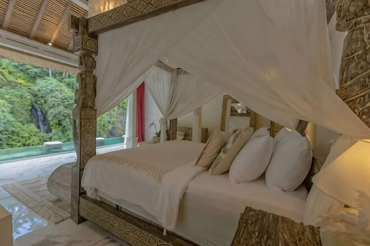 A four-poster bed with a canopy, a marble wall, and a view of greenery.
