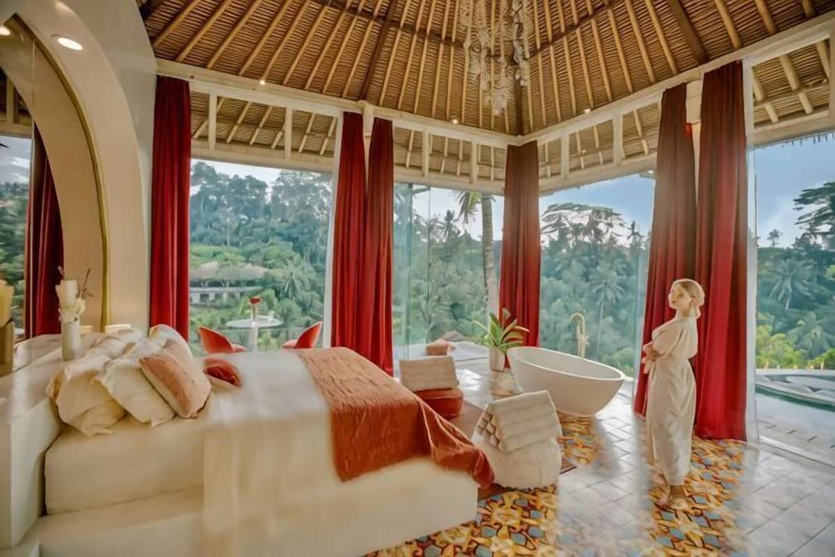 A bedroom with a bed, a bathtub, and a view of the outdoors.