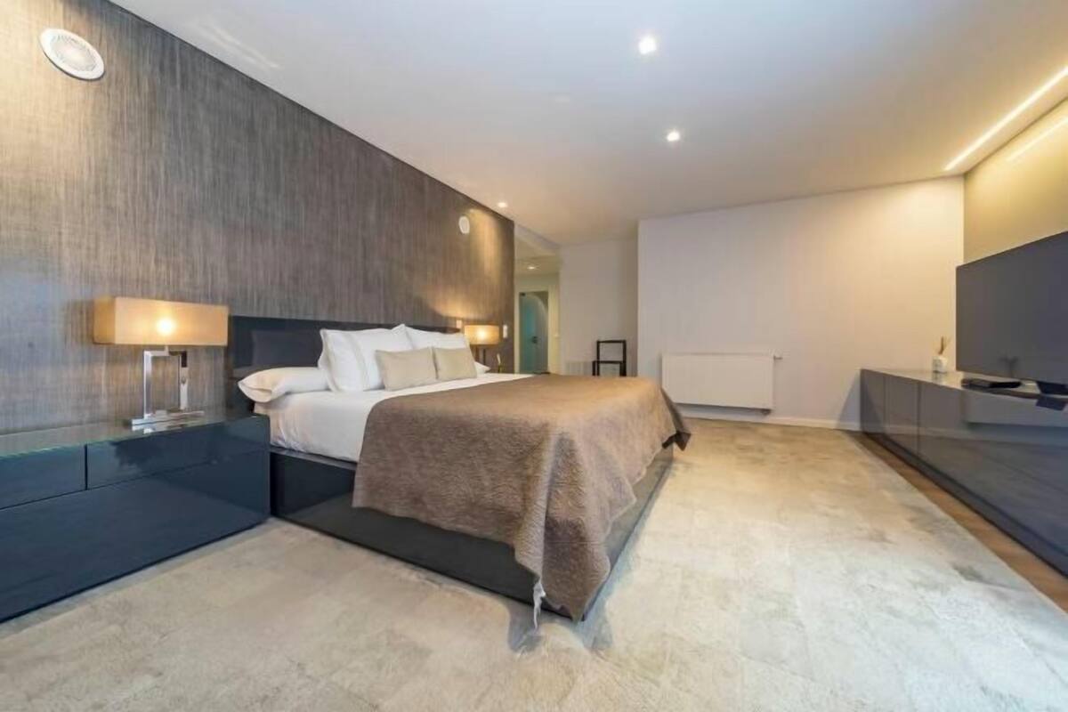 A modern bedroom with a bed, bedside tables, a TV, and a large mirror.