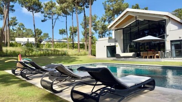 Ein modernes Haus mit Swimmingpool, umgeben von Bäumen und mit Gartenmöbeln.