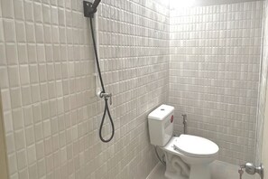 A bathroom with white tiled walls, a toilet, and a shower with a hose. - Tnn284 (Bangkok)
