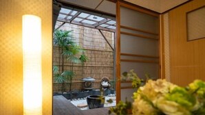 Ein traditionelles japanisches Interieur mit Tatami-Böden, Shoji-Schirmen und einem kleinen Garten mit Steinlaterne und Bonsai-Bäumen.