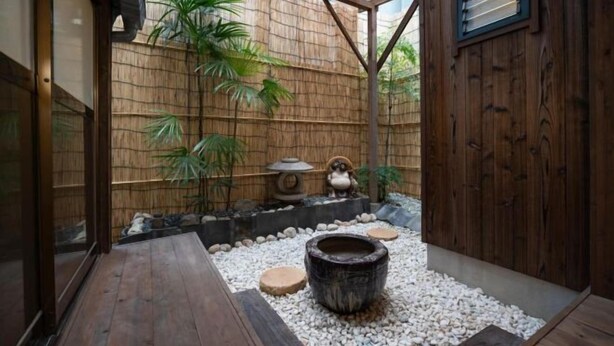 Ein traditioneller japanischer Garten mit einer Holzterrasse, einer Bambuswand und einem Steinbecken.