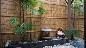 Ein Bambuszaun, ein Steinlaternen und eine Panda-Statue in einem Garten.