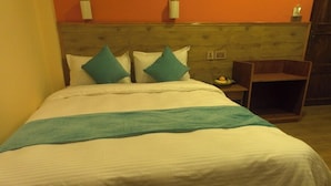 A bed with white bedding and teal pillows, a wooden headboard, and a small wooden nightstand with a fruit bowl. - Hotel Paya Nepal (Kathmandu)