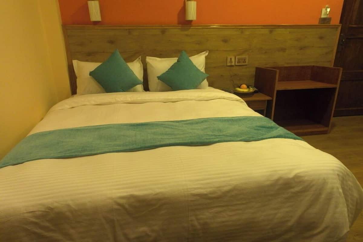 A bed with white bedding and teal pillows, a wooden headboard, and a small wooden nightstand with a fruit bowl.