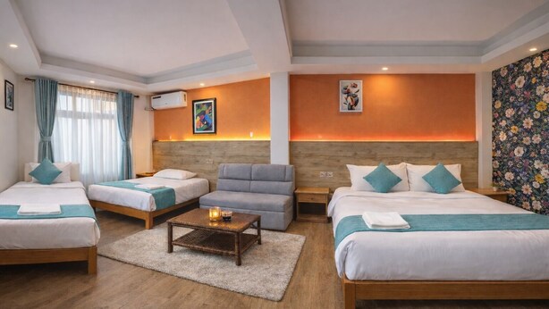 A hotel room with two beds, a sofa, a coffee table, and a floral wallpaper. - Hotel Paya Nepal (Kathmandu)