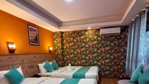 A hotel room with two beds, a sofa, a wooden floor, a floral wall, and an air conditioning unit. - Hotel Paya Nepal (Kathmandu)