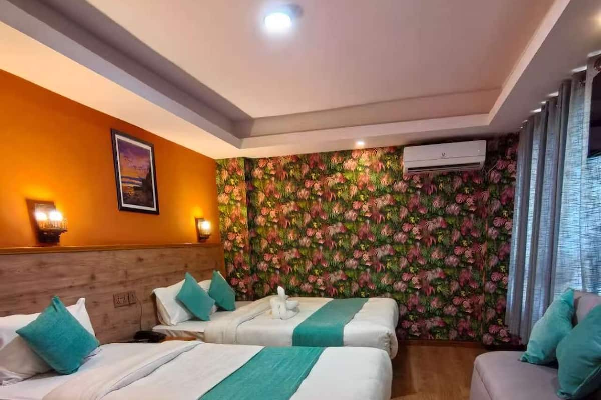 A hotel room with two beds, a sofa, a wooden floor, a floral wall, and an air conditioning unit.