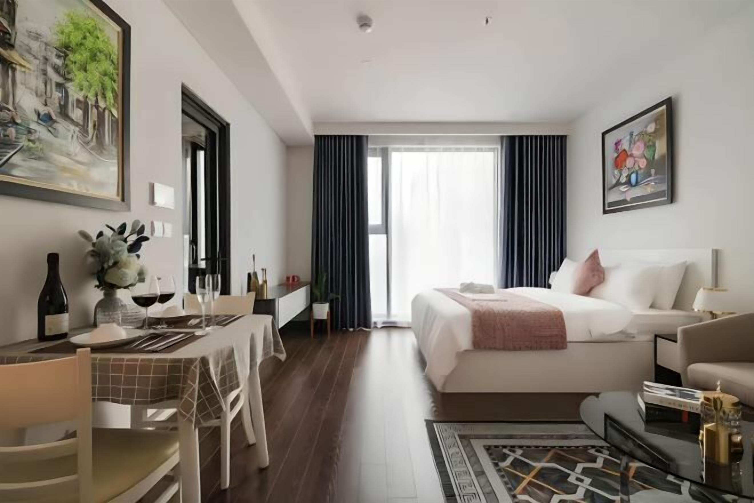 A hotel room with a bed, a desk, a chair, a dining table, and a large window.
