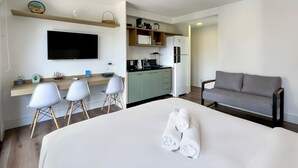 A modern hotel room with a large bed, a sofa, a desk with chairs, a kitchenette, and a TV. - Carinas 301 By WeCare (São Paulo)