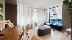 A modern living room with a wooden dining table, a sofa, and a large window with curtains. - Carinas 301 By WeCare (São Paulo)