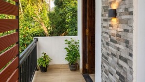 Un balcón con baranda de madera, dos plantas en macetas, un muro de piedra con una lámpara y una puerta.