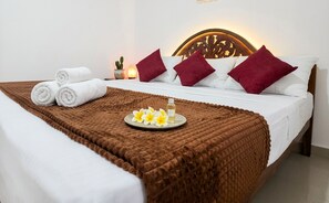 Un lit bien fait, avec des draps blancs, une couverture marron et un plateau sur lequel on a disposé des fleurs et une bouteille.