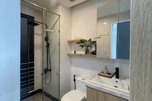 Une salle de bain moderne avec une douche à l’italienne en verre, des toilettes blanches, un meuble-lavabo en bois avec un évier et un miroir au-dessus du meuble.