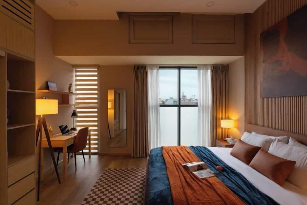 Une chambre d’hôtel avec un lit, un bureau, une chaise et une grande fenêtre avec des rideaux.