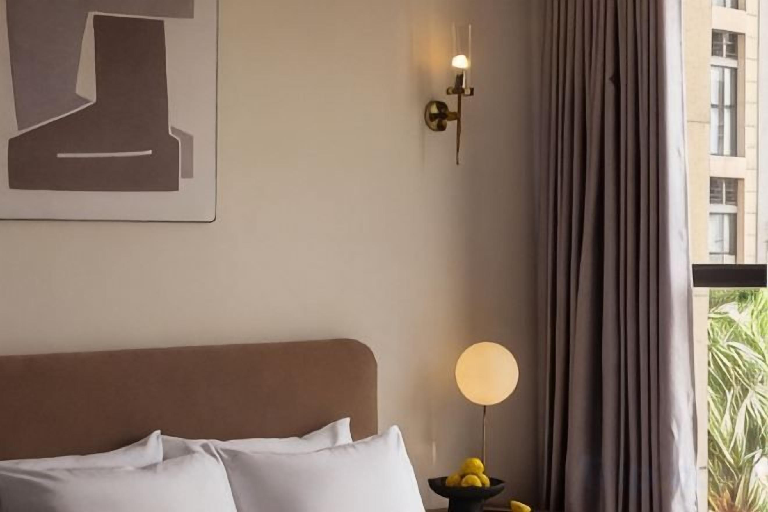 A hotel room with a bed, a wall-mounted light fixture, and a window with curtains.