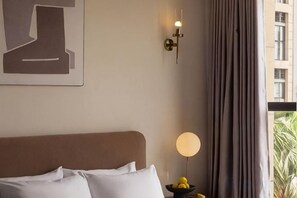 Una habitación de hotel con una cama, una lámpara de pared y un ventanal con cortinas.