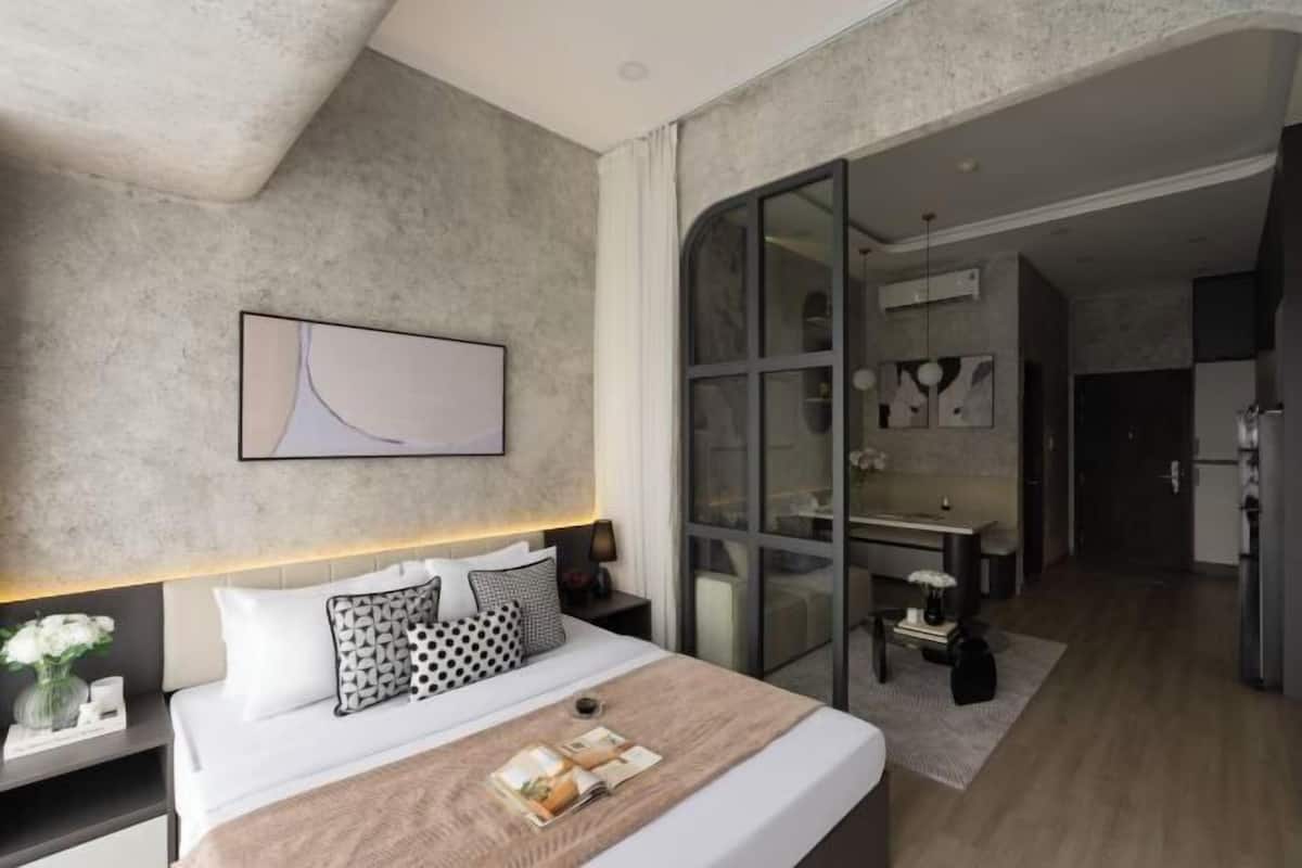 Une chambre d’hôtel moderne avec un grand lit, une table de chevet ornée d’un vase de fleurs, une œuvre d’art accrochée au mur et une porte-fenêtre coulissante donnant sur un coin repas.