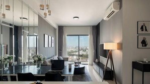 Habitación de hotel moderna con zona de comedor, sofá, lámpara de pie y un amplio ventanal con vistas.