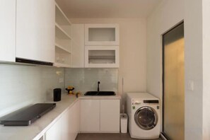 Cocina compacta con armarios blancos, lavadora y una pequeña encimera.