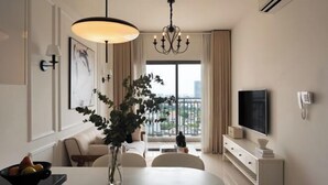 Una sala de estar moderna con una mesa de comedor, sillas, una araña, un televisor y un ventanal con vista a la ciudad.