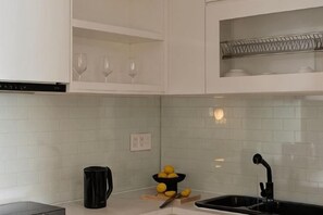 Een keuken met witte kastjes, een zwarte spoelbak en een witte betegelde achterwand.