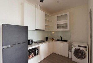 Une cuisine de taille réduite avec des meubles blancs, un réfrigérateur noir, un lave-linge et un évier.