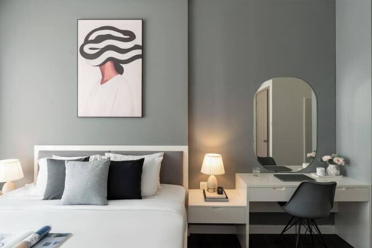 Une chambre à coucher comprenant un lit, une table de chevet, une lampe, un miroir et une œuvre d’art accrochée au mur.