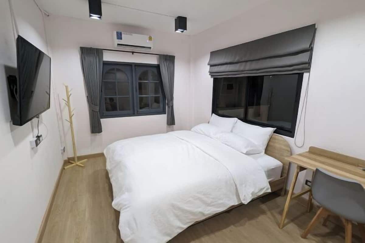 Un dormitorio con cama, escritorio, silla, televisor y ventana con cortinas.