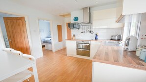 A compact kitchen with a built-in oven, a microwave, and a kettle. There is a dining area with a white table and chairs. - Swallows Croyde 3 Bedrooms, Sleeps 6, Beach Chale (Braunton)