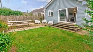 Una casita con patio, cerca de madera y jardín cubierto de césped.