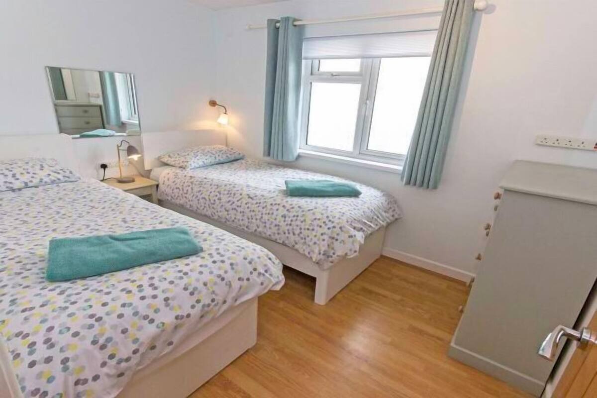 Un dormitorio con dos camas, un espejo, una lámpara de noche, una ventana con cortinas y un armario.