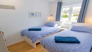 Un dormitorio con dos camas, una mesita de noche, una lámpara y una ventana con cortinas.