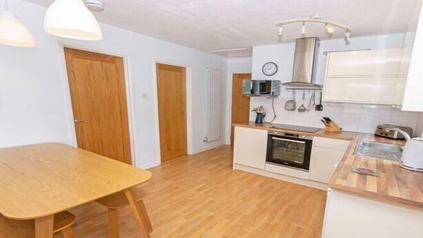 A compact kitchen with wooden flooring, a dining table, and basic appliances. - Swallows Croyde 3 Bedrooms, Sleeps 6, Beach Chale (Braunton)