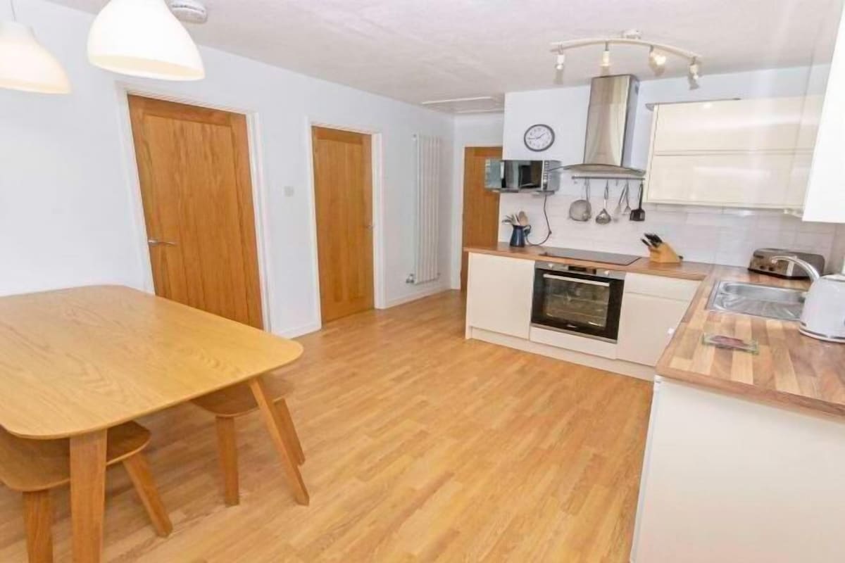 A compact kitchen with wooden flooring, a dining table, and basic appliances.