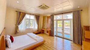 A hotel room with a bed, wooden flooring, a bench, and a sliding glass door leading to an outdoor area. - 4 bedroom Seafront Soan Villa - Sealinks Mui Ne (Phan Thiet)
