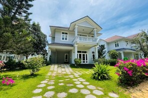 A two-story house with a front porch, a well-maintained lawn, and a pathway leading to the entrance. - 4 bedroom Seafront Soan Villa - Sealinks Mui Ne (Phan Thiet)