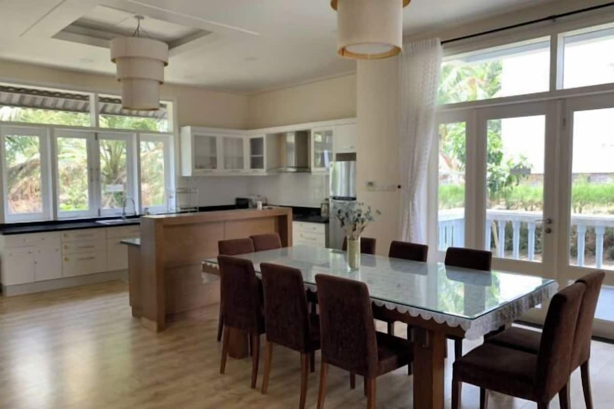 A spacious kitchen with a dining area, large windows, and a view of greenery.