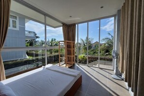 A bedroom with a large bed, a view of a pool, and a balcony with a fan. - 4 bedroom Seafront Soan Villa - Sealinks Mui Ne (Phan Thiet)