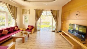 A spacious living room with a sofa, a coffee table, and a television on a wooden stand. - 4 bedroom Seafront Soan Villa - Sealinks Mui Ne (Phan Thiet)
