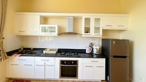 A compact kitchen with white cabinets, a microwave, a stove, an oven, and a refrigerator. - 4 bedroom Seafront Soan Villa - Sealinks Mui Ne (Phan Thiet)