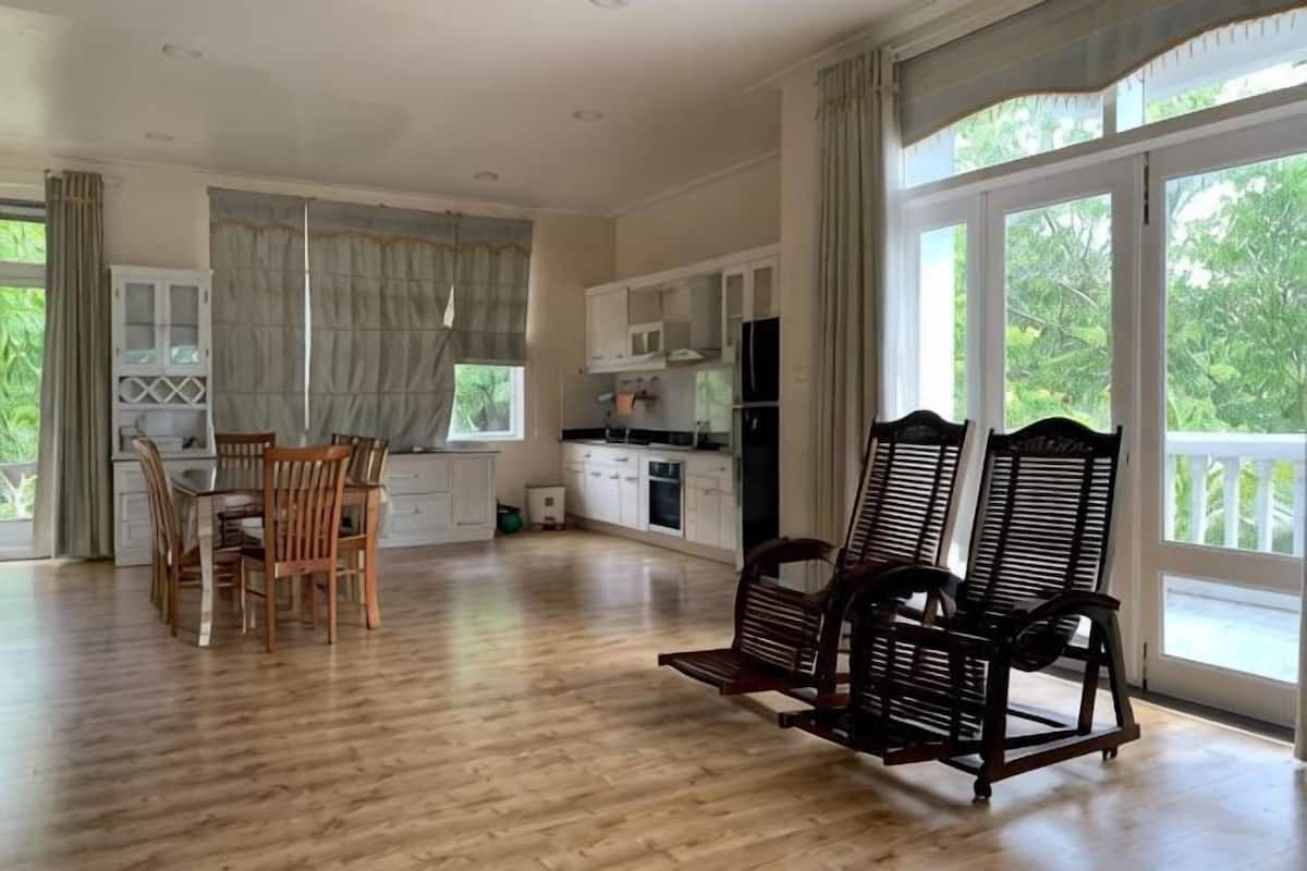 A spacious living area with a dining table, chairs, a sofa, and a kitchen in the background.