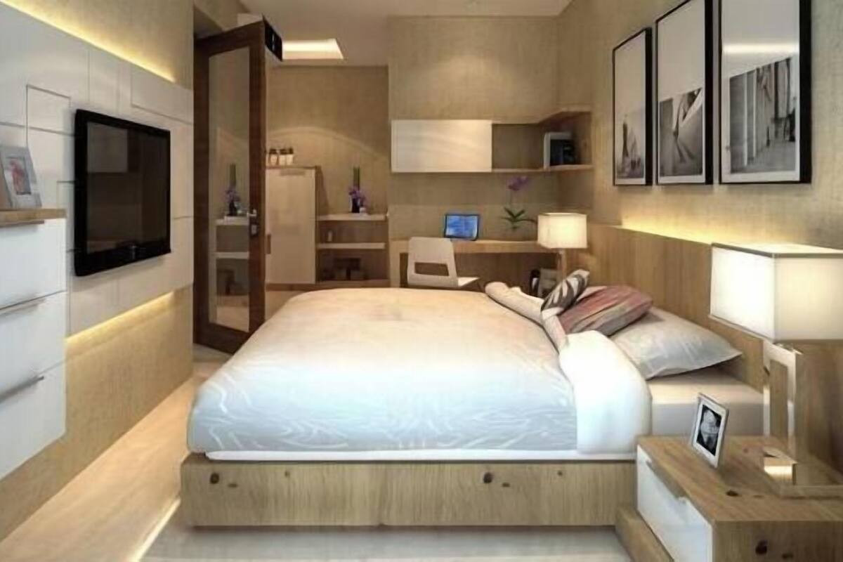 Une chambre à coucher moderne, avec un lit, des tables de chevet, un bureau, une chaise, un téléviseur et des tableaux encadrés accrochés au mur.