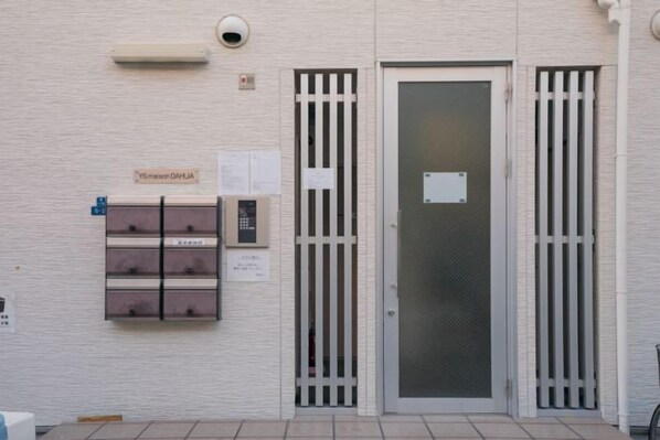 A building entrance with a glass door, a security camera, a mailbox, and a set of keys on the wall.