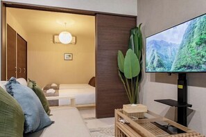 A modern hotel room with a bed, a TV mounted on the wall, and a wooden side table with a plant. - YS Maison｜Direct train to Tsutenkaku, Shinsekai, and Shinsaibashi in 5 minutes (Osaka)