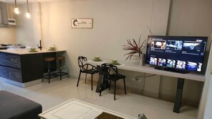 En moderne stue med spiseplads, en køkkenø og et fladskærms-tv på væggen.